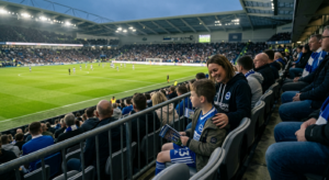 A professional, cinematic shot of a young fan and their parent sitting in a football stadium, captur