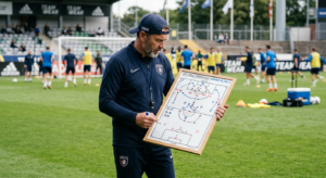 A professional editorial shot of a soccer coach standing on the pitch during a training session, foc